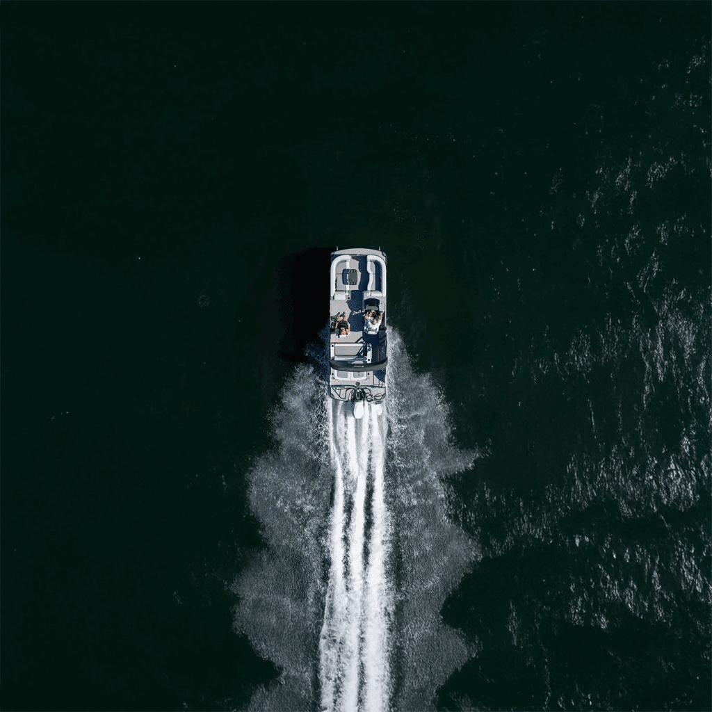 A top-down view of a speedboat leaving two white trails of wake as it speeds away from the marina through dark water.